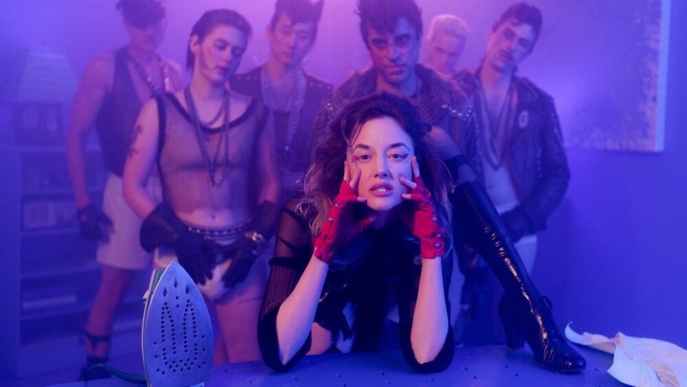 Suze surrounded by men in Please Baby Please